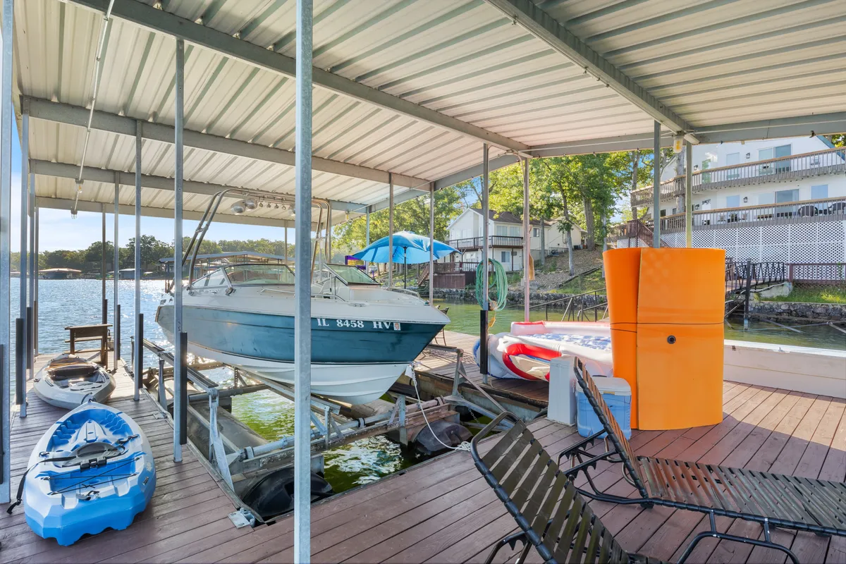 A lively lakefront setup featuring a boat, multiple kayaks, and colorful chairs arranged on the dock. The water shimmers in the background, clearly inviting guests to embark on a kayaking or boating trip. The scene feels vibrant and full of potential for lakeside fun.