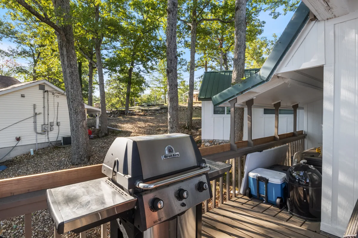 An inviting exterior shot of a deck area featuring a grill, surrounded by tall trees and adjacent to nearby buildings. The space is set up for barbecuing, outdoor dining, and socializing—a perfect backdrop for group celebrations and relaxed outdoor evenings.