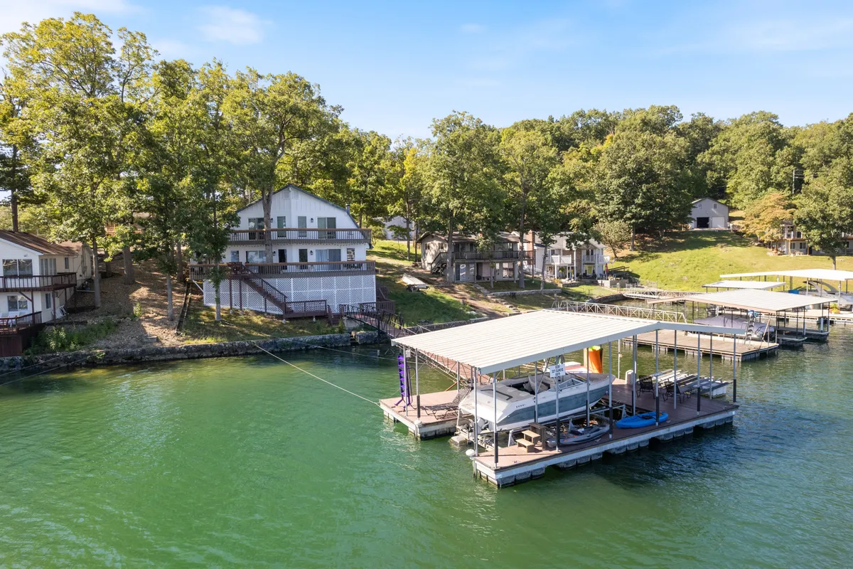A peaceful lakeside scene featuring multiple boathouses and private docks stretching out over calm water, framed by lush trees on both sides. The setting is quiet, inviting, and perfectly suited for fishing, boating, or simply relaxing by the shore. The expansive water surface and absence of crowds underscore the sense of privacy and tranquility.