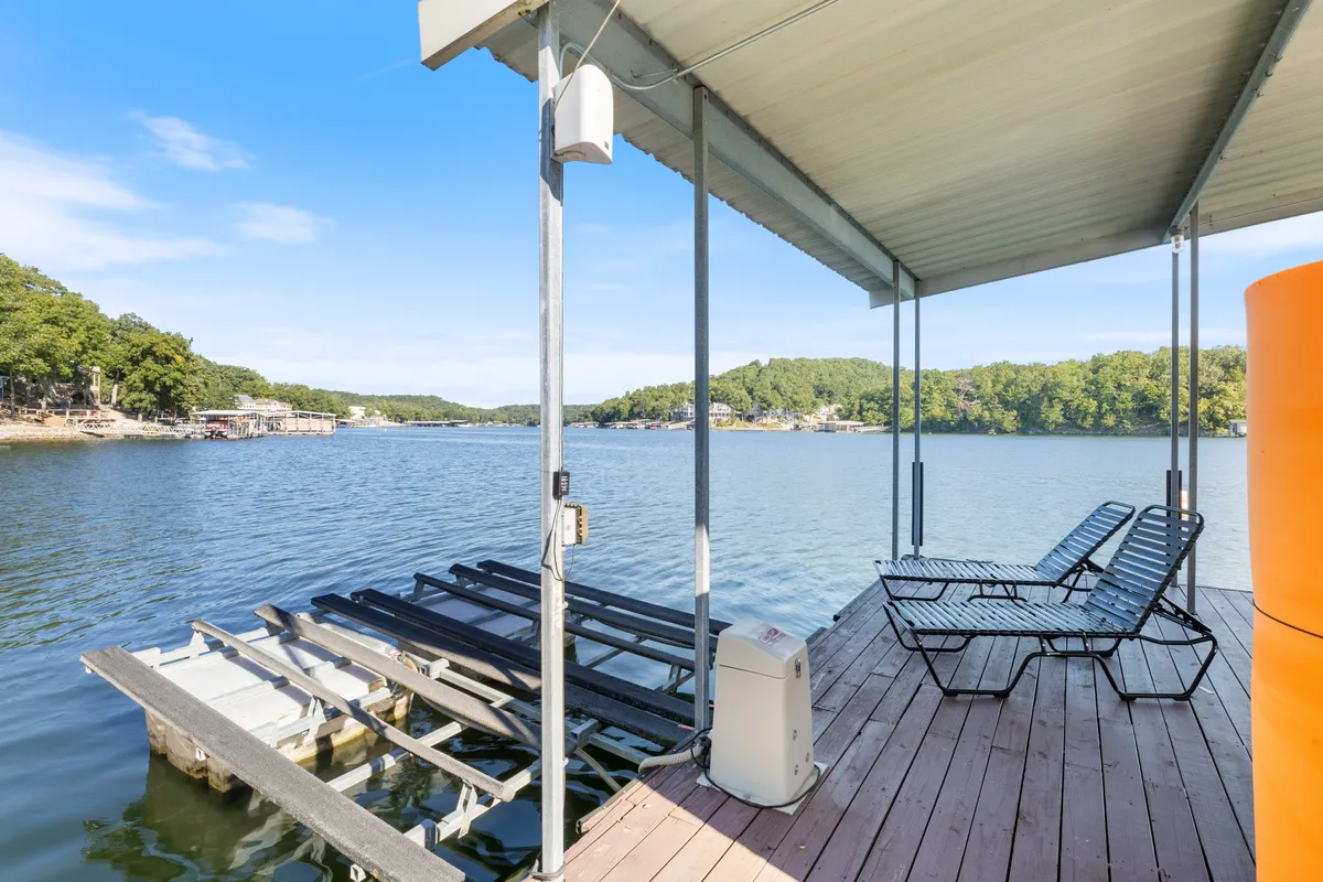 This exterior image showcases a dock stretching out over a serene lake, complete with lounge chairs and surrounded by lush trees. The tranquil water and natural setting evoke the perfect atmosphere for lakeside fun, including sunbathing, boating, and relaxing with friends after a day of adventure.