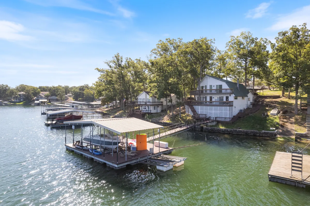 A wide shot of a dock extending into a serene lake surrounded by trees and houses, perfect for boating, fishing, swimming, or simply relaxing by the water. The dock and open water invite families and groups to jump in or set out on a kayak adventure.