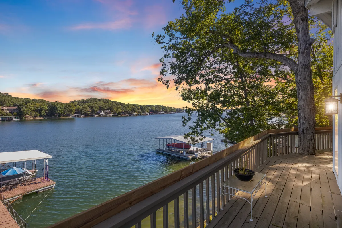 The image showcases a serene lake view from the property’s spacious deck, overlooking a private dock surrounded by lush trees and set against a vibrant sunset sky. The tranquil water is perfect for boating and fishing, while the inviting deck is ideal for relaxing, sipping morning coffee, or enjoying evening barbecues with family and friends.
