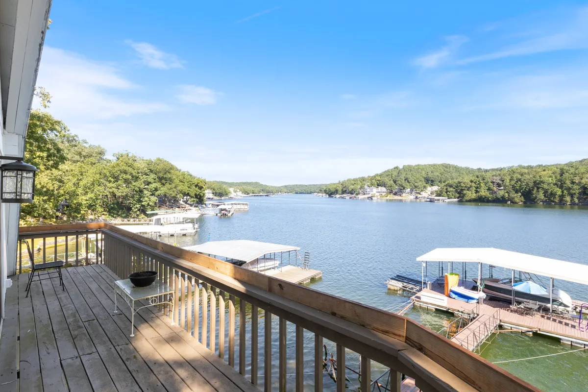 A wide lake view with docks and a spacious wooden deck in the foreground, bordered by trees. The tranquil waters invite visitors to fish or launch a boat, and the scene is set for a sunrise adventure or a relaxing afternoon by the lake.