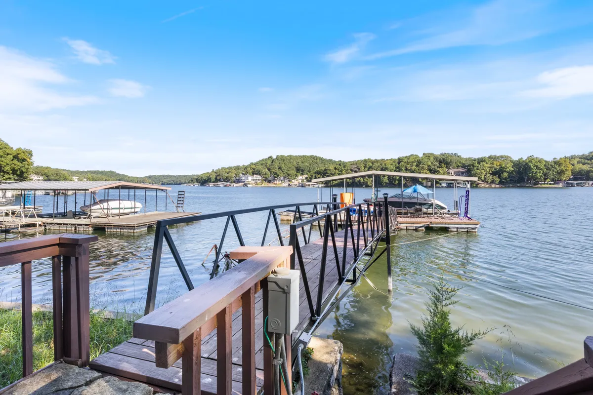 A wooden dock extends over the calm lake, with boats tied up and lush greenery in the background. The water is inviting, and evening sunlight casts a soft glow across the scene. There is a sense of relaxation and readiness for water activities like fishing or kayaking.